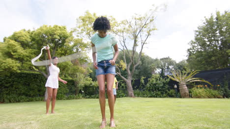 Feliz-Madre-Afroamericana-Saltando-Con-Su-Marido,-Su-Hija-Y-Su-Hijo-En-Un-Jardín-Soleado,-En-Cámara-Lenta