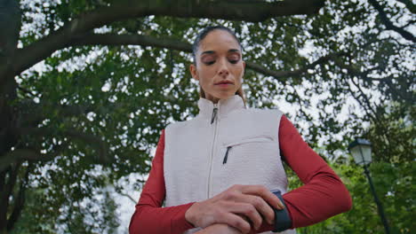 fitness girl looking smartwatch at daily training in green lush park closeup.