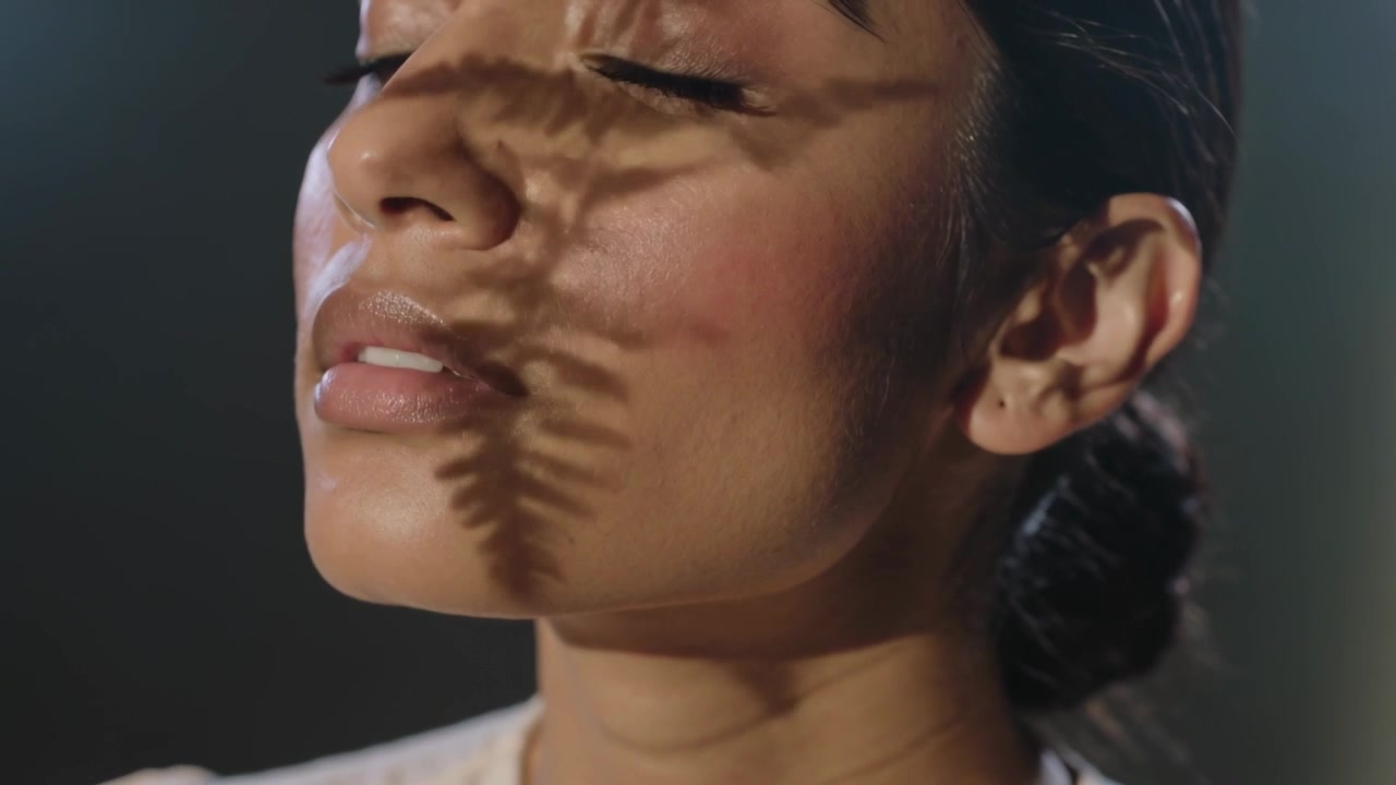 Luce in movimento che proietta un'ombra di felce su una donna in un ritratto in studio, che alza il mento e indossa una camicetta chiara.
