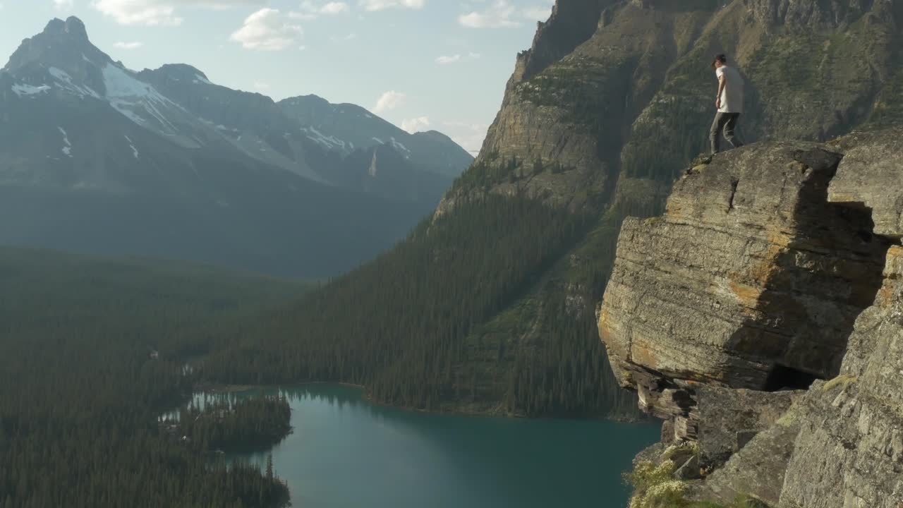 un hombre camina hasta el borde de un acantilado para disfrutar de la vista del lago ohara