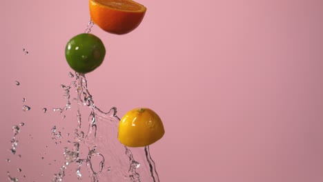 citrus fruits and water fly through the air in front of a pink background