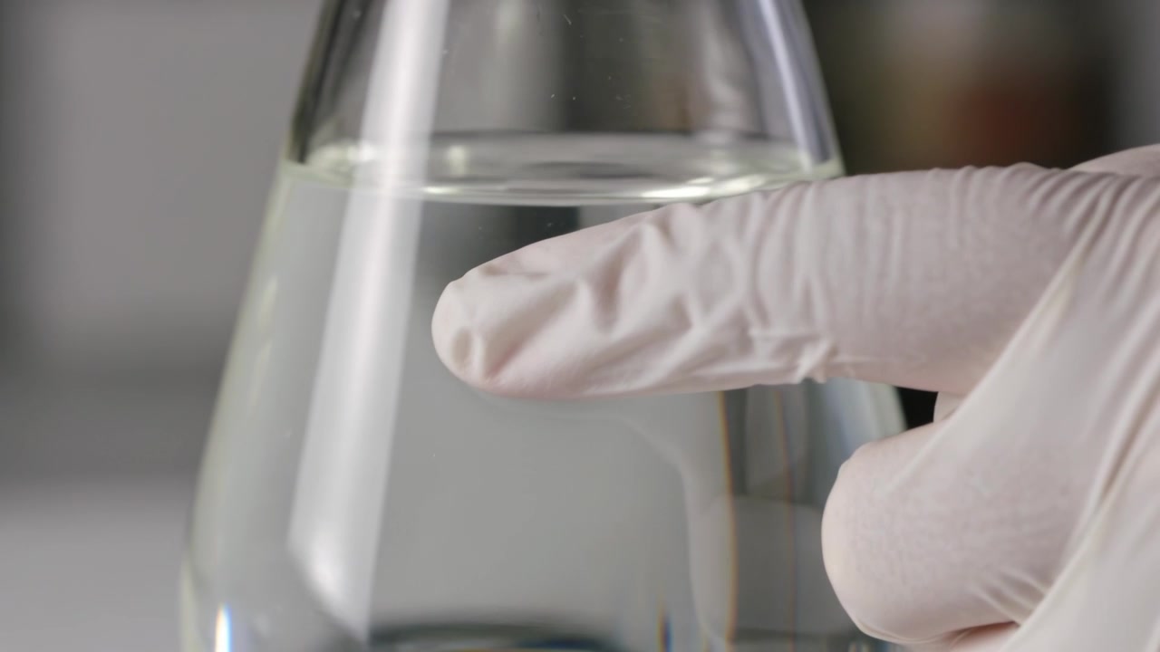 Polpastrello guantato che tocca e spinge una microbolla su un becher conico di vetro sul banco del laboratorio, rimuovendo la bolla.