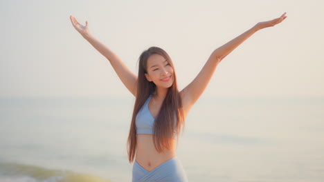 a fit, young, asian woman in activewear, extends her arms over her head in a yoga pose