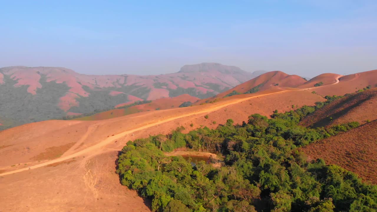 Drone che si muove lateralmente seguendo un sentiero di fango su una collina con colline ondulate sullo sfondo