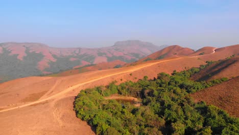 Drone-moving-sidewards-following-a-mud-path-on-a-hill-with-rolling-hills-in-the-background