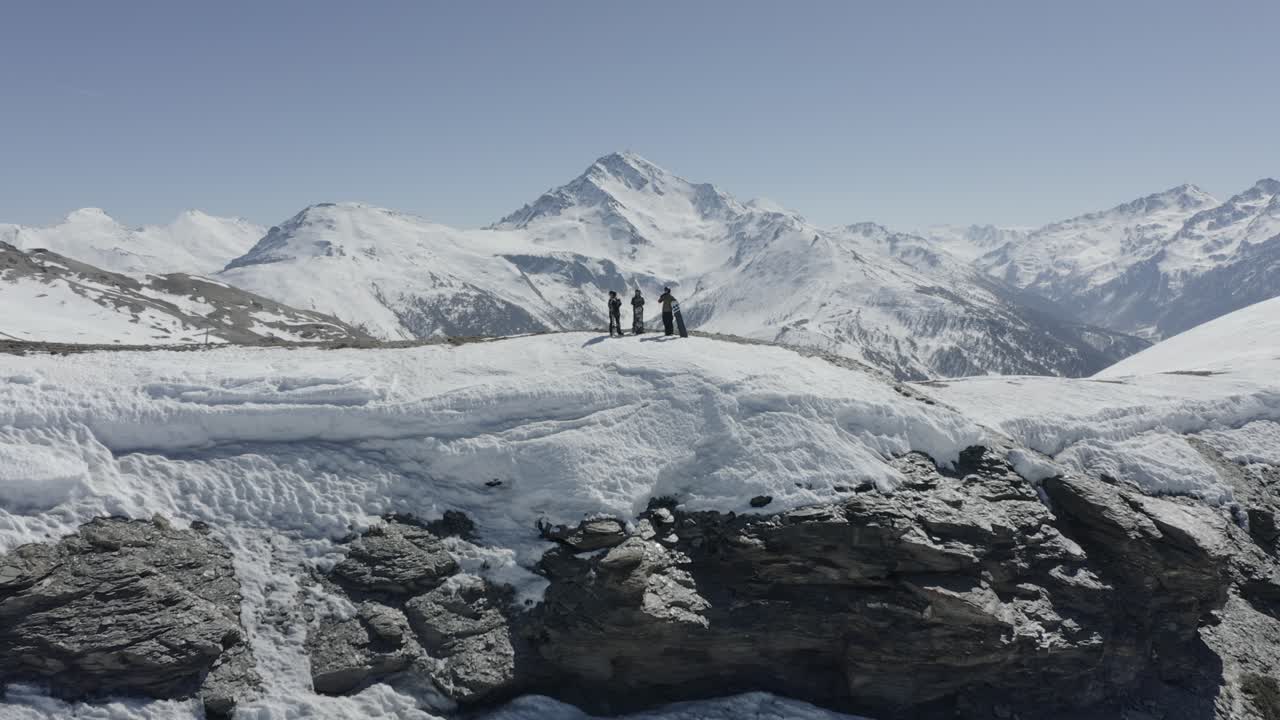 Three people standing on a snowy mountain ridge with majestic peaks in the background