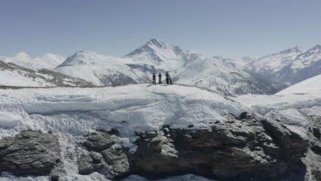 three people standing on a snowy mountain ridge with majestic peaks in the background