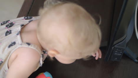 a baby girl in a summer overall examining the tv screen