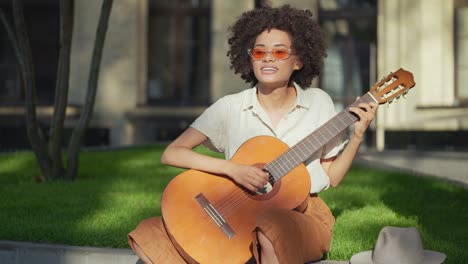 artista callejero de cabello rizado sonriente tocando la guitarra acústica y cantando, pasatiempo