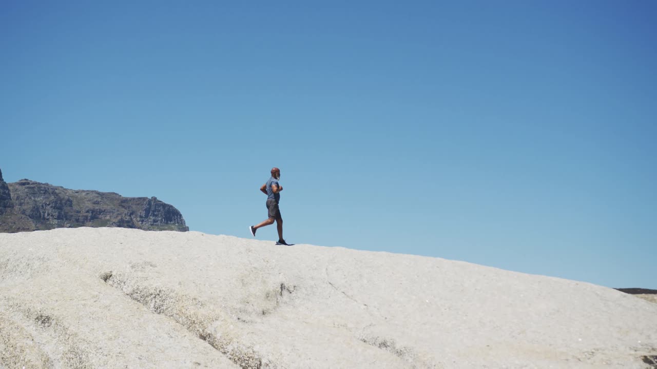 시니어 아프리카계 미국인 남자가 바 ⁇ 가의 바위 위에서 달리기를 연습하고 있습니다.