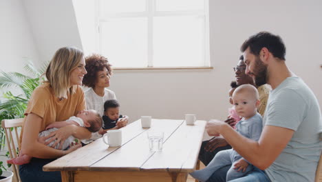 two families with babies meeting and talking around table on play date at home