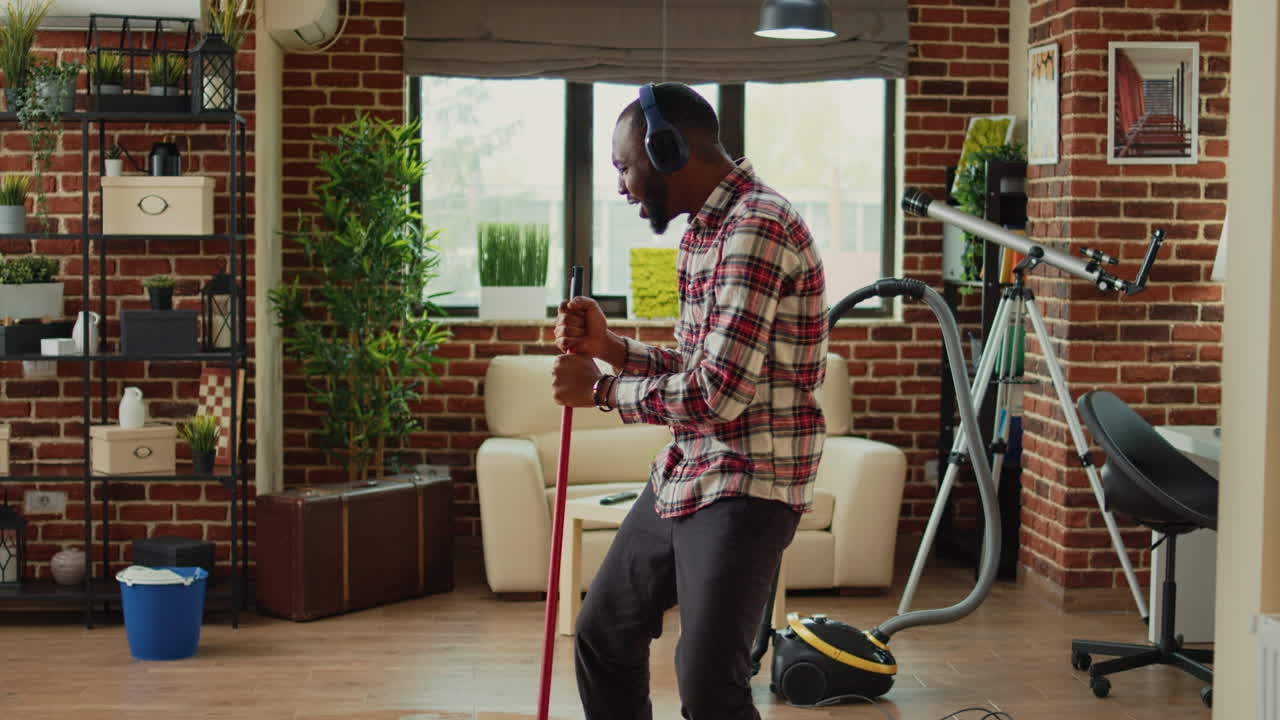Cheerful funny boyfriend using mop to clean wooden floors