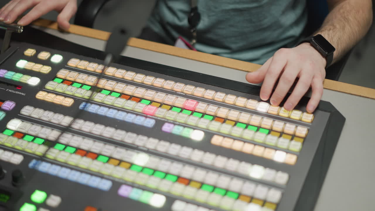 Close-up shot of hands operating professional video switcher, controlling camera feeds and transitions in control room, advanced broadcasting equipment, TV production environment, studio control
