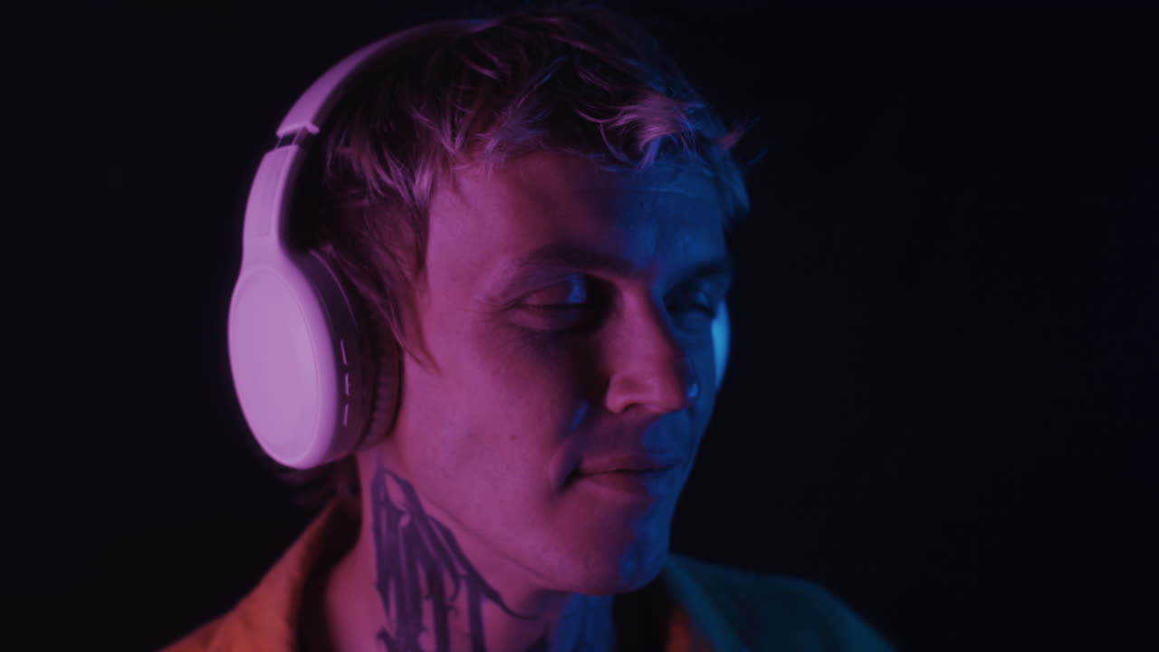 Guy with Tattoo on Neck Dancing to Music in Room with Neon Light