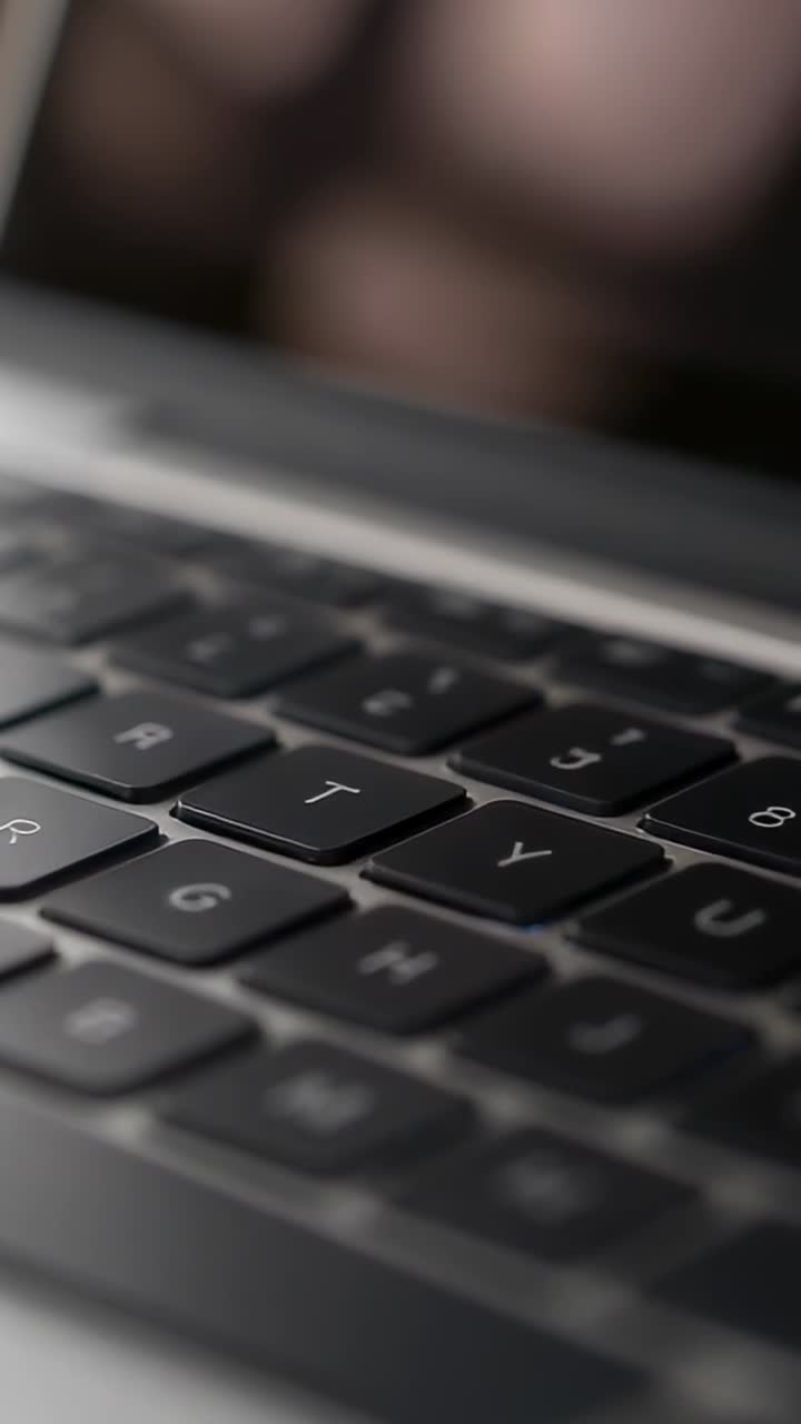 Vertikal video: Kamera fokuserer og afslører tastaturet på en bærbar computer på skrivebordet, viser tasterne G H T Y U.