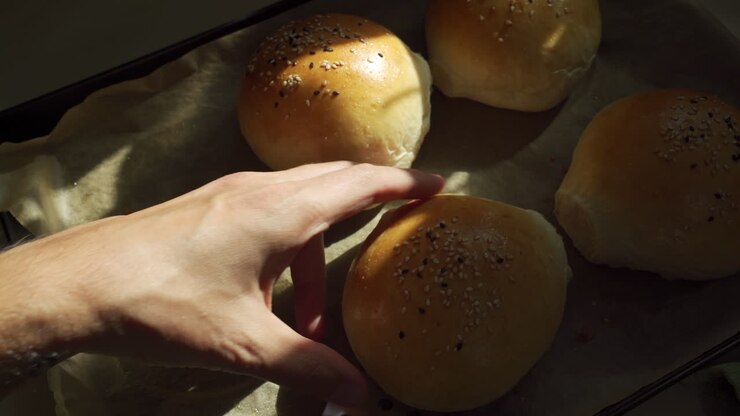 Beautiful and freshly made burger buns are being taken out of oven and the chef move them into a cooling rack