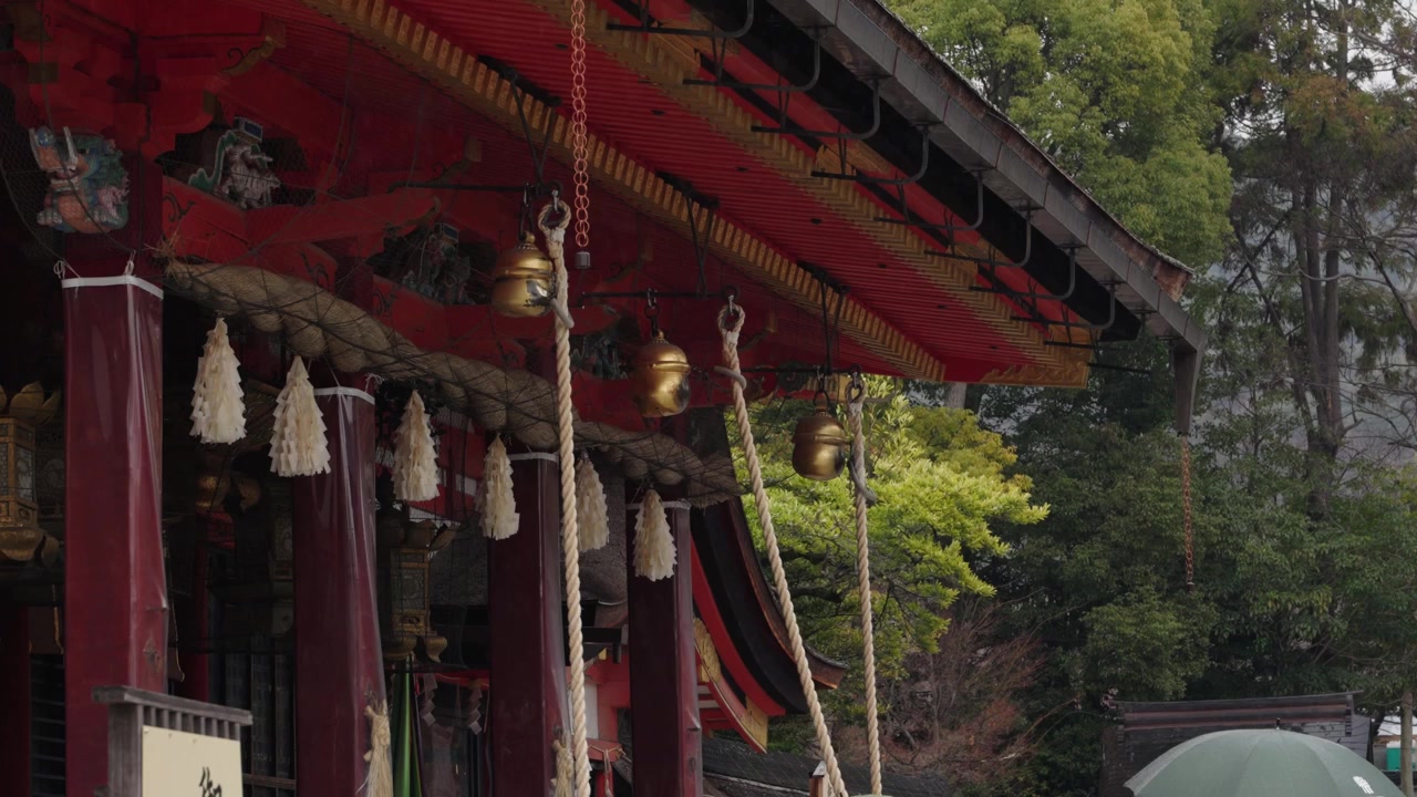Gyldne klokker på kæder og snoede reb hænger fra en udsmykket rød helligdomsfacade ved Fushimi Inari Kyoto, Japan.