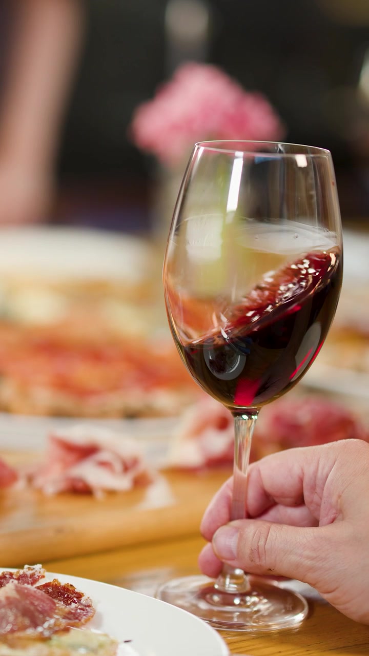 Una mano mescola delicatamente vino rosso in un bicchiere su un tavolo di antipasti italiani.