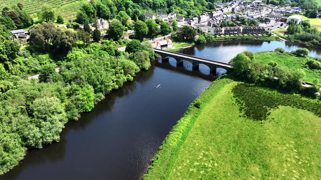 Aerial view of a scenic river with an arch bridge and a village, featuring a boat