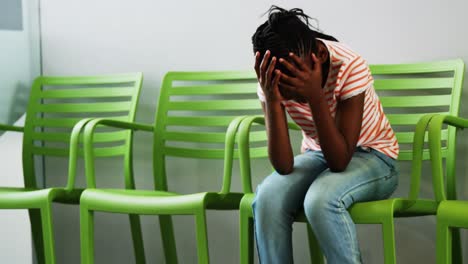 upset girl sitting on chair in hospital corridor