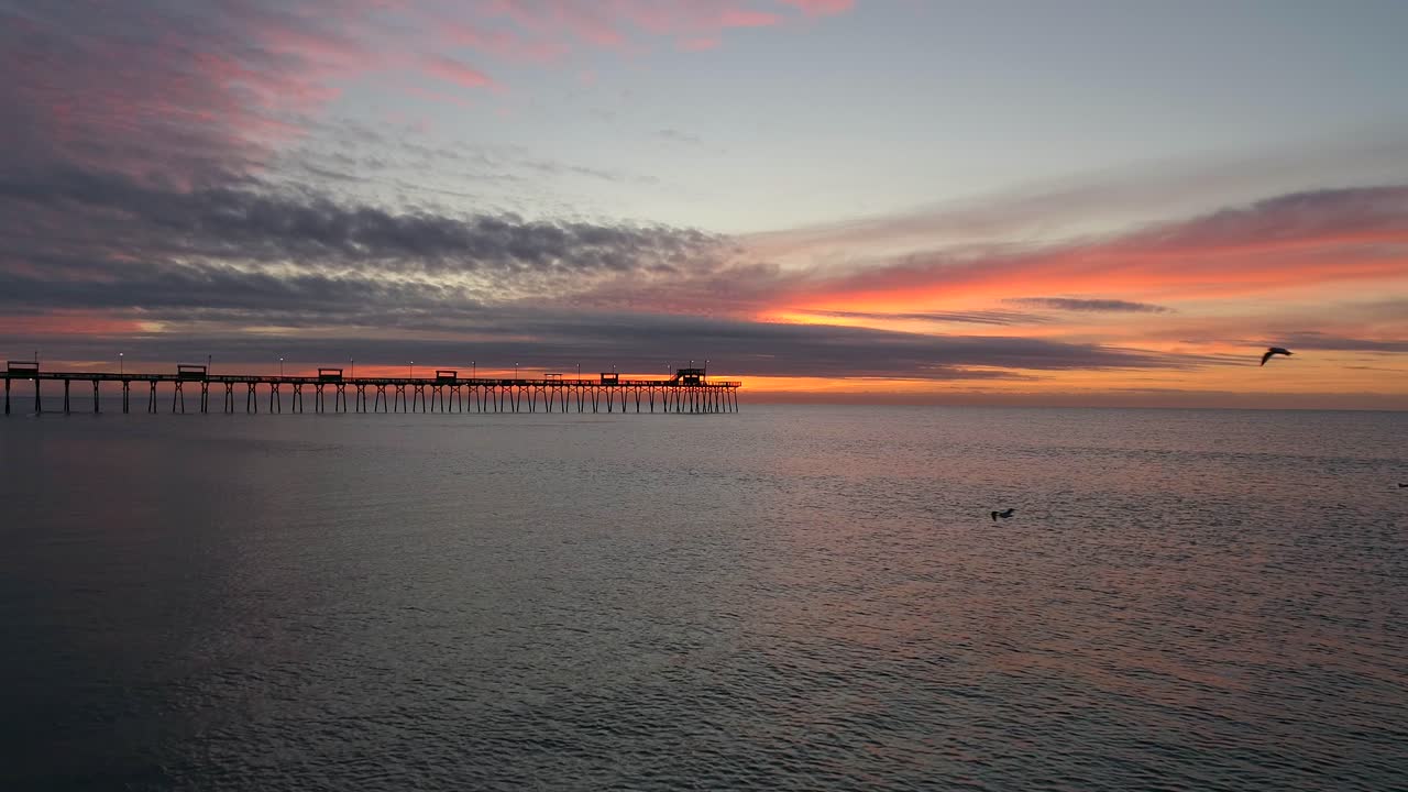 에메랄드 섬 해안에 있는 보그 인렛 부두를 향한 공중 드론 전망, 노스캐롤라이나의 햇살 가득한 화려한 새벽과 일출에 날아다니는 새들