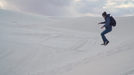 Joven-Juguetonamente-Corre-Y-Salta-Al-Lado-De-Una-Pequeña-Duna-De-Arena,-Cámara-Lenta