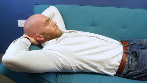 hombre acostado en un sofá relajándose con las manos detrás de la cabeza