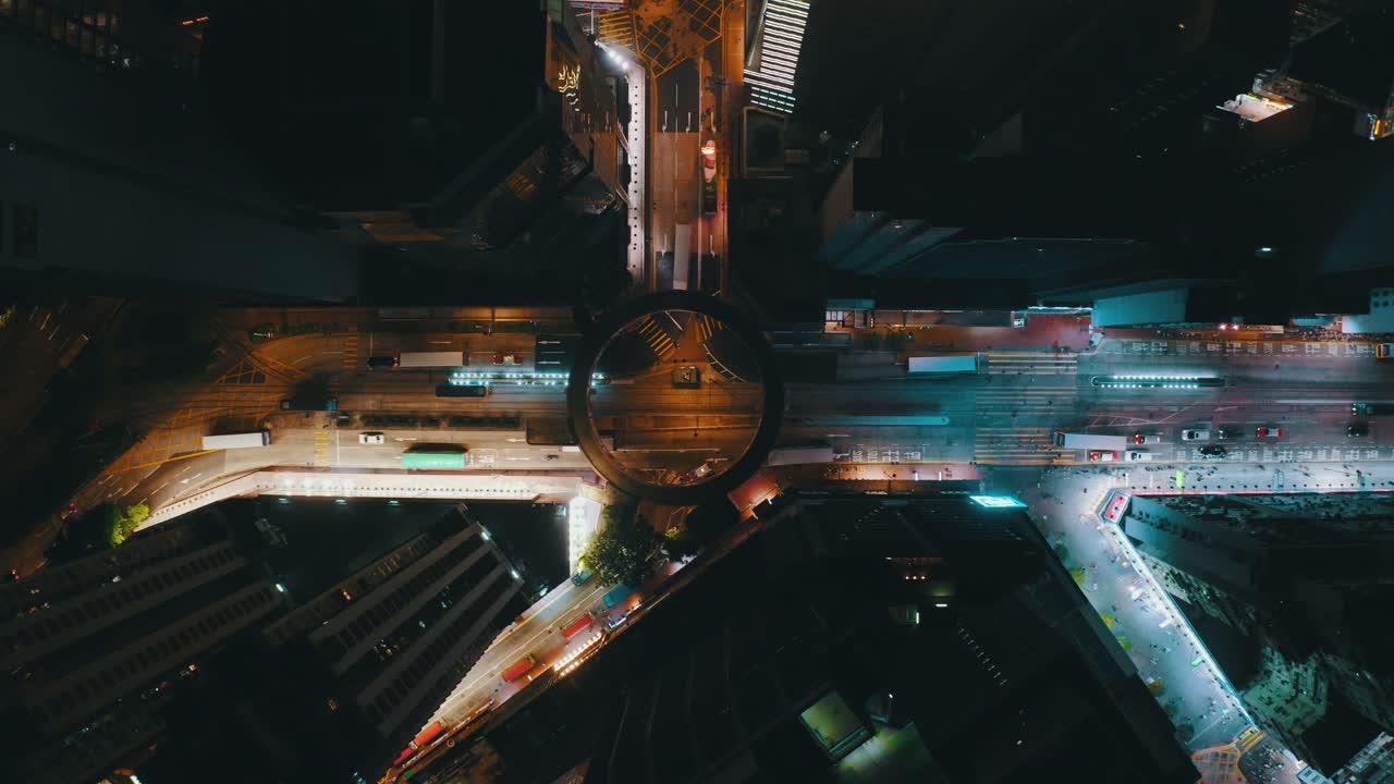 Drone shot traveling downward in the middle of a city toward a circle shaped crossroad during the night. the traffic is heavy with bus and cars
