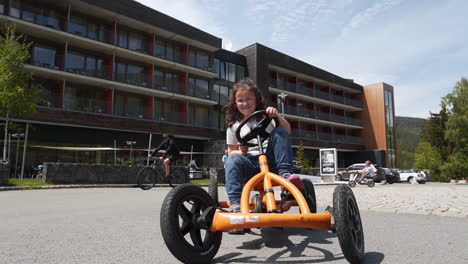 tiro fhd giratorio de una niña pequeña montando un cuadriciclo de pedal naranja y zigzagueando en una carretera asfaltada en un complejo privado en dolní morava, república checa