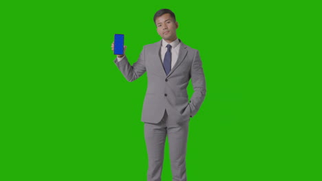 Studio-Shot-Of-Smiling-Businessman-In-Suit-Holding-Blue-Screen-Mobile-Phone-Against-Green-Screen-2