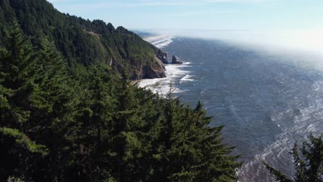 Crane-drone-shot-revealing-waves-crashing-on-the-breathtaking-Oregon-coast-from-behind-towering-trees