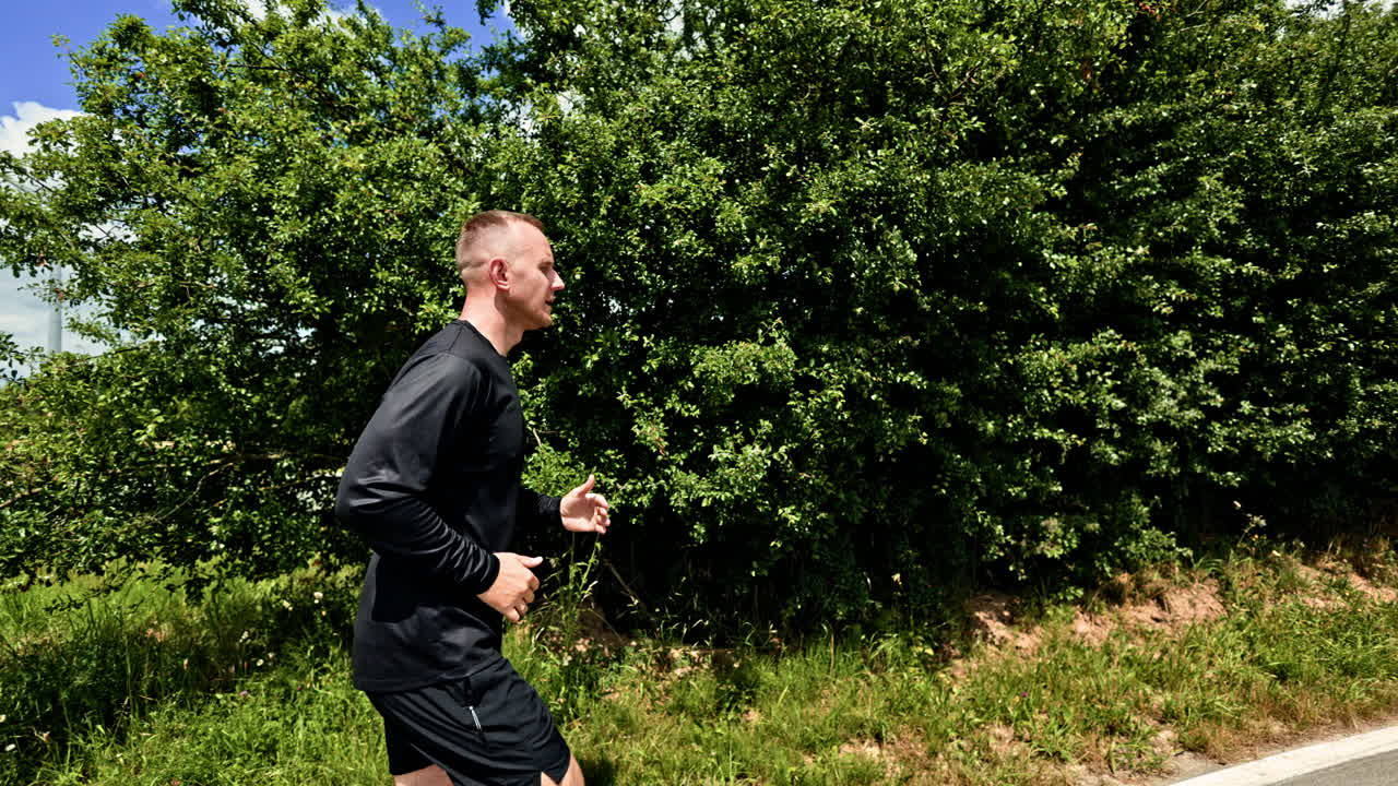 Homem corredor atlético, forte e saudável ao ar livre. Jovem em uma corrida matinal em um dia ensolarado. Treino cardiovascular ao ar livre. Estilo de vida saudável. Homem de shorts pretos e camiseta.