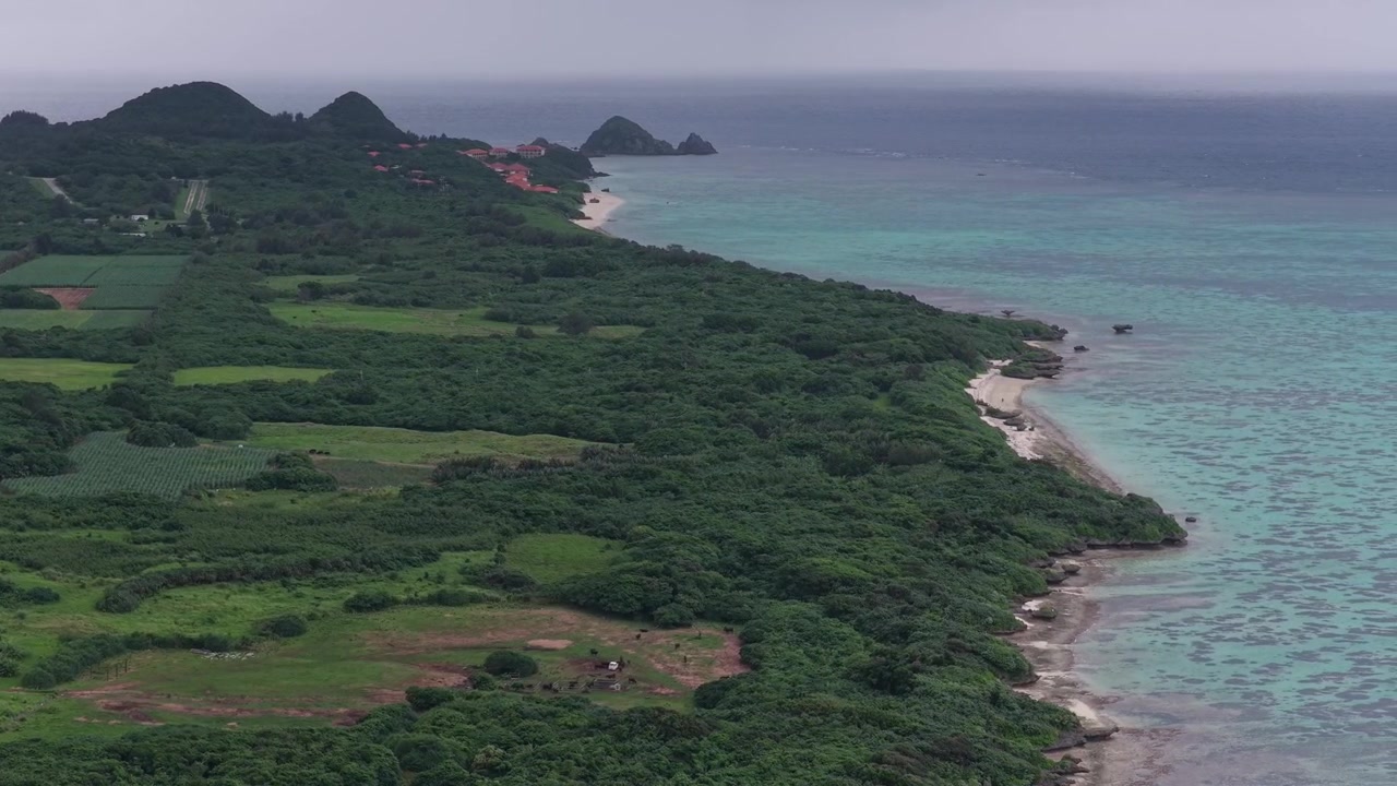 Japonya, Okinawa, Ishigaki Adası, Kabira Koyu yakınlarındaki Kojima Adası'nın yemyeşil kıyı şeridi, tarım arazileri ve turkuaz sularının üzerinde sağa doğru hareket eden yatay havadan çekim