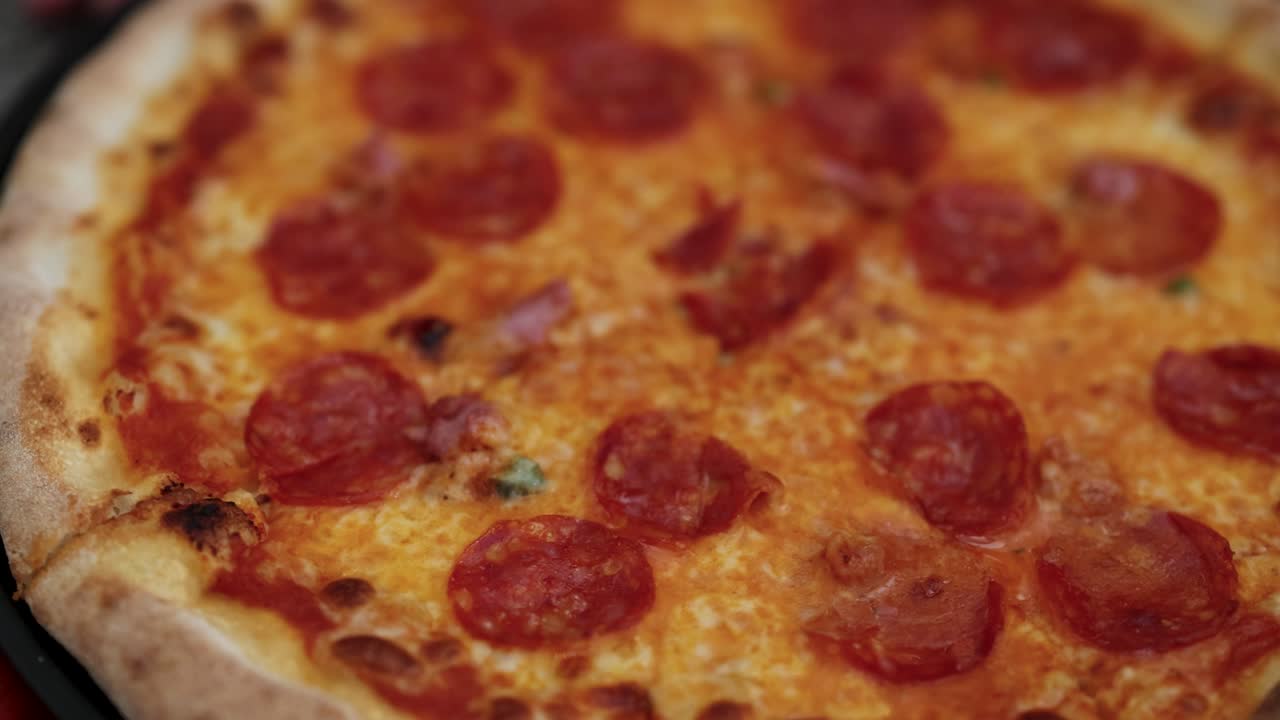 페페로니 피자가 회전하는 클로즈업 뷰, 따뜻한 조명 속에서 토핑과 질을 보여줍니다.