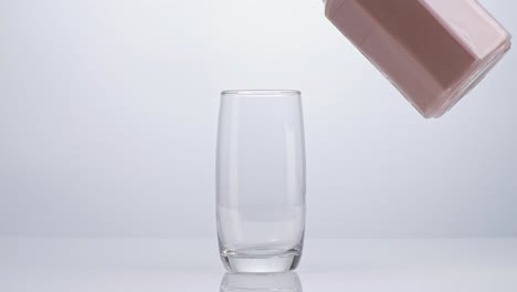 movimiento lento verter bebida de leche de chocolate en vaso de vaso sobre fondo blanco