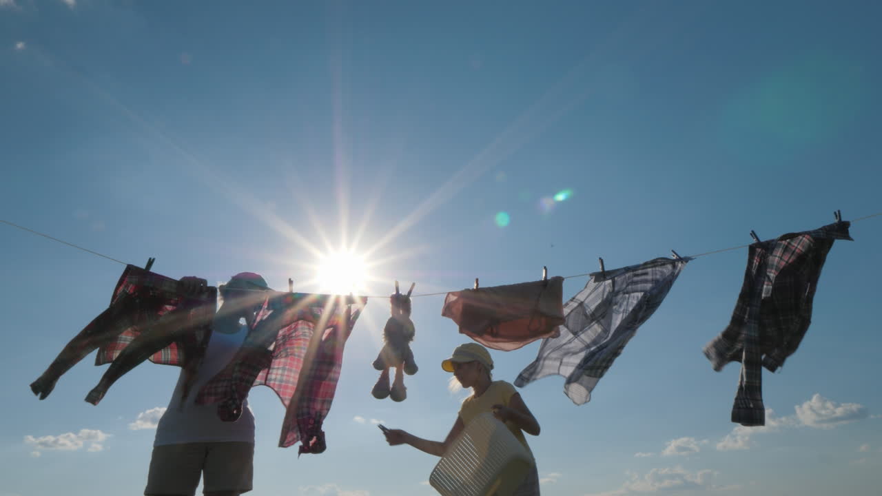 딸은 엄마가 건조를 위해 옷을 걸도록 도와줍니다.