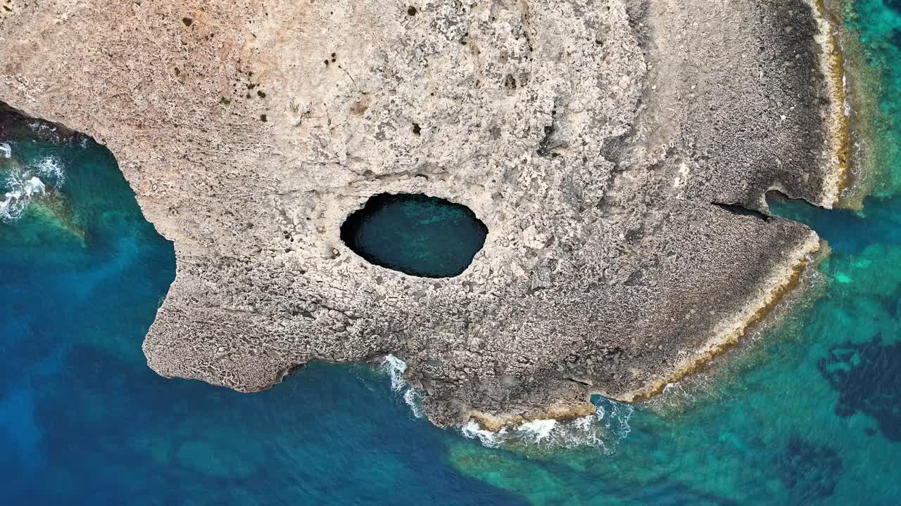 Una ripresa aerea con drone rivela l'apertura circolare in calcare della Laguna di Corallo a Mellieħa, Malta, con acqua di mare turchese circondata da una costa rocciosa e frastagliata