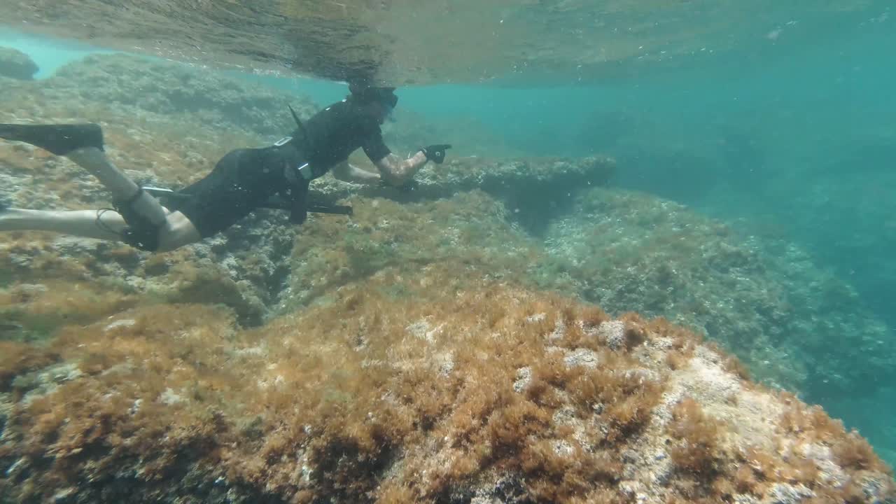 Spearfisher tries to catch a fish at rocky sea floor in the mediterranean sea