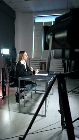 long-haired woman sitting at desk talking and gesturing. soffits light the blogger recording a video. vertical video.