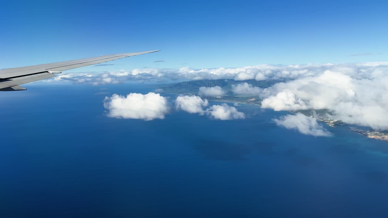 Udsigt fra flyvindue, der viser Oahus kystlinje, blåt hav, skyer og vinge