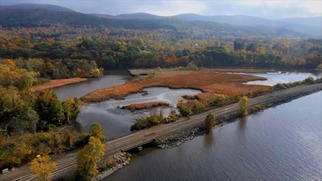 a scene with a river, train tracks, marshland swamps, mountains, hills, and autumn foliage