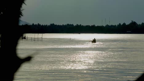 an abstract silhouette shot of a local thai fisherman paddling a boat towards the bank of the chanthaburi river, in the distance the beautiful morning sunrise reflecting off the water, thailand