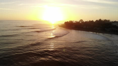 Drohnenaufnahmen-Aus-Der-Luft-Am-Rincon-Point-Surf-Break-Mit-Wellen-Und-Menschen,-Die-Bei-Sonnenuntergang-An-Der-Kalifornischen-Golden-Coast-Zum-Strand-Surfen