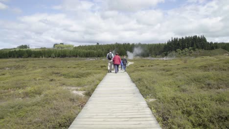 Un-Disparo-Siguiendo-A-Una-Familia-Mientras-Caminan-Por-Un-Sendero-De-Madera-En-Los-Cráteres-De-La-Luna-En-Taupo,-Nz