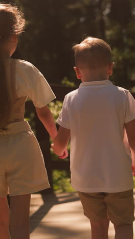 el hermano pequeño y la hermana caminan de la mano a lo largo de una pasarela de madera en el bosque. niños felices pasan las vacaciones de verano en el campo. niños en el parque