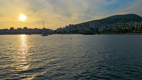 Timelapse-Del-Atardecer-De-Saranda:-La-Bahía-De-La-Ciudad-Costera-Se-Transforma-Bajo-El-Brillo-Dorado,-Revelando-La-Tranquila-Belleza-De-Los-Barcos-En-El-Puerto