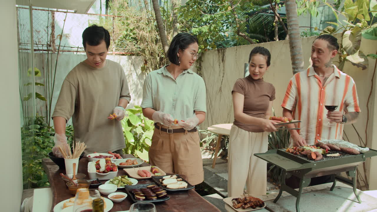 Friends Helping Each Other when Barbecuing Outdoors