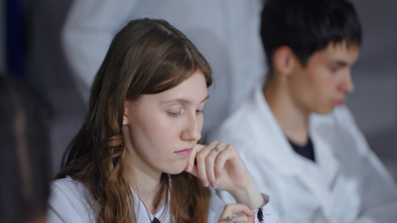 한 젊은 여성 학생이 교실의 책상에 앉아서 손에 정벌레를 들고 아래를 바라보고 있습니다.