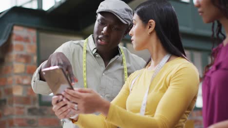 Happy-diverse-fashion-designers-wearing-tape-measures-discussing-work-using-tablet-at-office