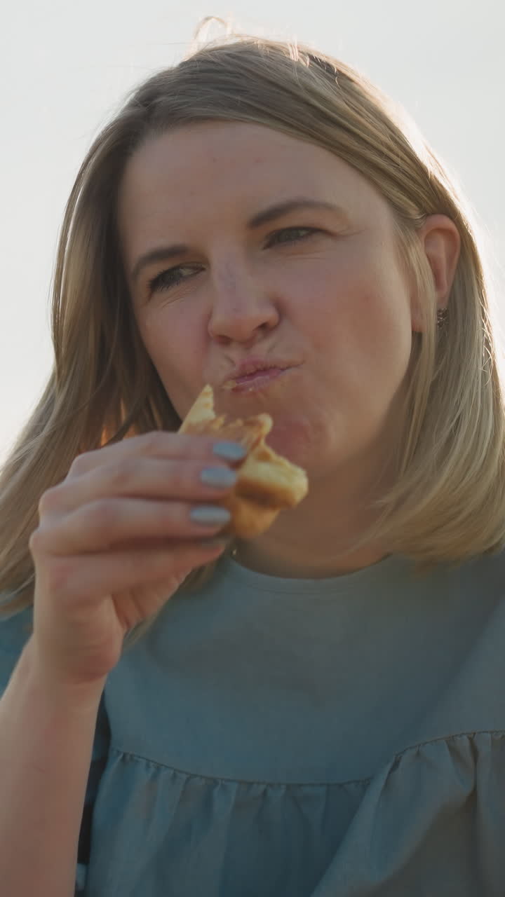un niño pequeño con una camisa blanca se sienta en un campo cubierto de hierba, compartiendo un perrito caliente con su madre, que está vestida de azul. ella toma un bocado y se lo devuelve a él, capturando un tierno momento de intercambio